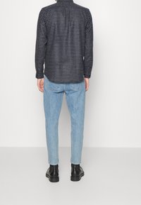 Camicia button-up in una fantasia a quadri blu scuro, il tessuto appare testurizzato; abbinata a jeans azzurri a gamba stretta e stivaletti neri. 