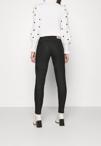 Czarne legginsy o gładkiej fakturze, dopasowanym kroju i wysokim stanie, zestawione z białym swetrem z czarnymi groszkami na rękawach.