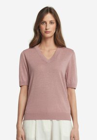 Ljusrosa kortärmad tröja med V-ringning. Mjuk textur och ribbad fåll. Åtsittande design med lätt puffärmar.