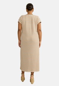 Abito maxi in crema con motivo geometrico marrone, maniche corte, scollatura rotonda e lunghezza sotto il ginocchio; abbinato a sandali con platform.