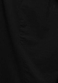 Svart tyg med en texturerad mönster med små upphöjda prickar, som visar släta och något skrynkliga områden, vilket skapar visuell djup.