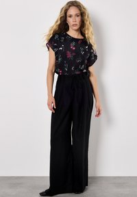 Haut noir à fleurs avec des manches courtes roulées, associé à un pantalon noir à jambe large taille haute, avec une taille nouée et un tissu fluide.