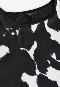 Svartvit mönstrad T-shirt med rund halsringning, mjukt tyg och abstrakt penseldesign. Etiketten visar "NEXT."
