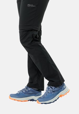 Blue hiking shoes with orange accents, paired with black technical pants. Shoes feature textured uppers and rugged rubber soles for traction.
