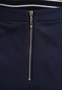 Jupe bleu marine avec une fermeture éclair argentée, un tissu texturé, et un design épuré avec une taille visible et une forme simplement structurée.