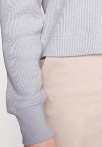 Lichtgrijze cropped sweater met ribbelstructuur en aansluitende manchetten, gecombineerd met een zachtroze broek. Eenvoudig ontwerp en neutraal kleurenpalet.