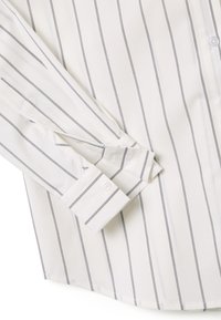 Camisa blanca de manga larga con finas rayas verticales negras, puño abotonado visible en la manga doblada, textura de tela de algodón.