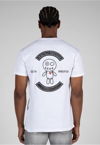 White cotton t-shirt featuring a black graphic design on the back, depicting a character with button eyes, stitched mouth, and a heart tattoo.