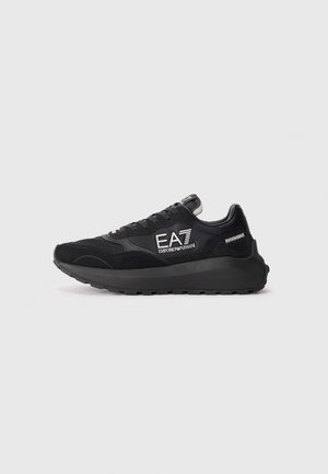 Black sneaker with mesh and suede material, featuring a thick sole, lace-up design, and logo accents on the side.
