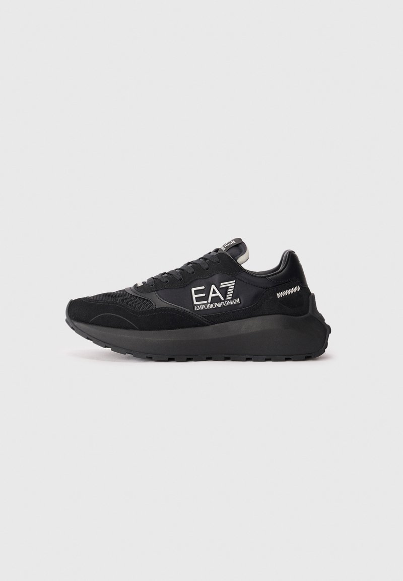 Zapatilla negra con material de malla y ante, que cuenta con una suela gruesa, diseño de cordones y acentos de logo en el costado.