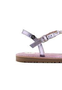 Sandal in metallo viola con suola piatta, cinturino alla caviglia regolabile e soletta testurizzata rosa chiaro. Presenta un accento con logo argentato.