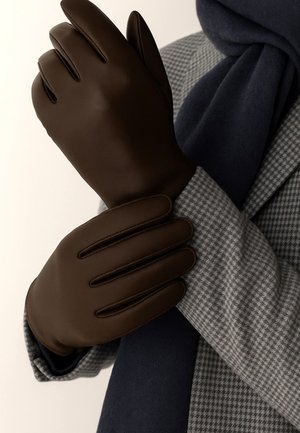 Brown leather gloves with stitched accents, featuring a smooth texture and a fitted design, worn over a gray patterned coat and navy scarf.