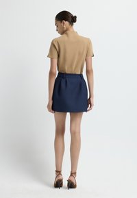 Beige poloshirt, marineblauwe gemarmerde mini-jurk, en bruine sandalen met hoge hakken, gezien van achteren tegen een lichte achtergrond.