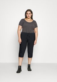 Donkergrijze top met korte mouwen, gecombineerd met zwarte cropped broeken met een trekkoord in de taille. Zwarte enkellaarsjes maken de outfit compleet.