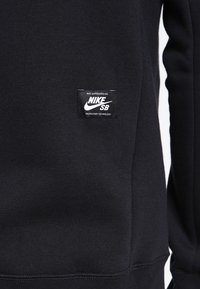 Černá mikina Nike SB s texturovanou tkaninou a vyšitým logem na hrudi, zdůrazňující odolnost a funkčnost.