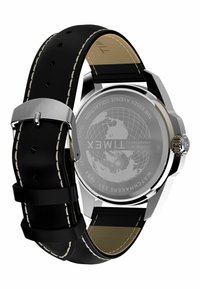 Hodinky Timex s kulatým pouzdrem z nerezové oceli, černým koženým páskem s bílým šitím a strukturálním sklem na zadní straně, které zobrazuje mapu světa.