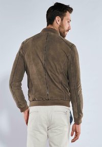 Braune Wildleder-Bomberjacke mit gerippten Bündchen und Saum, die kontrastierende Nähte und ein strukturiertes Rückenpanel aufweist. Figurbetonte Passform.