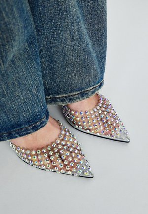 Szpilki z okrągłym noskiem, wykonane z przezroczystego plastiku i metalicznych akcentów, ozdobione wielokolorowymi kryształkami, zestawione z niebieskim dżinsem.