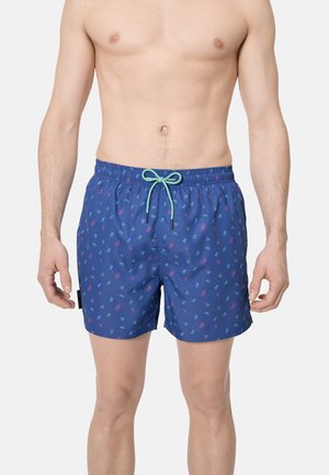 Hombre vistiendo pantalones cortos de baño azules con un pequeño patrón multicolor de bicicletas y un cordón de ajuste color verde azulado en la cintura.