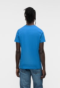 Μπλε βαμβακερό μπλουζάκι με κοντά μανίκια και στρογγυλή λαιμόκοψη, με λεία υφή. Φορεμένο με μπλε τζην από denim.