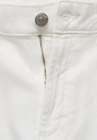 Tejido de mezclilla blanca con cierre de cremallera y botón plateado. La textura es suave con sutiles detalles de costura a lo largo de las costuras.