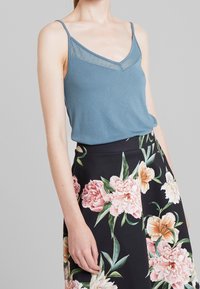 Ljusblå linne med tunna axelband och spetsliknande kant, parat med en svart blommig kjol med stora rosa och persika blommor.