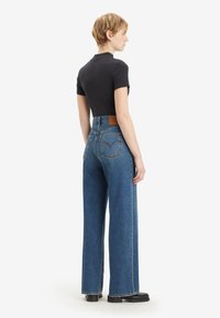 Hoge taille wijde jeans in middelblauwe denim met een tan leren patch, gecombineerd met een fitted zwart shirt met korte mouwen.