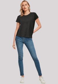 T-shirt noir à manches courtes avec un col rond, associé à un jean skinny bleu. La tenue est complétée par des baskets blanches.