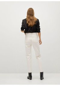 Blusa de satén negra con mangas enrolladas, pantalones blancos de cintura alta y botas negras de tobillo. Diseño sencillo, textura suave y ajuste a medida.