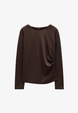 Brązowa bluzka z długim rękawem, o okrągłym dekolcie i subtelnym marszczeniu po bokach, na białym tle.