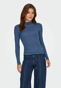 Blå ribbad långärmad topp med scalloped-halsringning och manschetter, figurnära design och mjuk textur, i kombination med högmidjade mörka denimjeans.