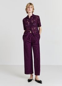 Top in pizzo viola con maniche corte e pantaloni larghi coordinati, dotati di vita con coulisse e un motivo floreale intricato. Ballerine nere.