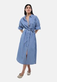 Robe chemise rayée bleue et blanche avec des manches longues, un devant à boutons, une taille ceinturée et une fente sur le côté ; fabriquée en tissu de coton léger.