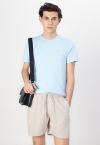 Ελαφρύ μπλε βαμβακερό T-shirt, κοντά μανίκια; μπεζ λινές βερμούδες με ελαστική μέση; μαύρη υφασμάτινη τσάντα χιαστί με ρυθμιζόμενο λουρί.