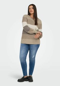 Beige and gray striped knit sweater with a V-neck, paired with blue slim-fit jeans and black slip-on shoes. Soft texture, oversized fit.