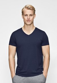 Navy blue v-neck t-shirt made of cotton, featuring short sleeves and a soft texture, worn with gray sweatpants in a neutral background.