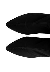 Bottes noires en daim à bout pointu avec une texture lisse, des coutures visibles et une silhouette élancée. Convient pour une tenue formelle ou sophistiquée.