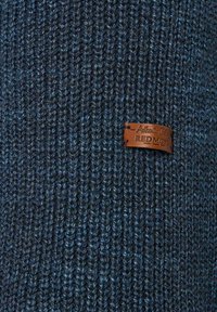 Strickmütze aus Wolle in dunklen Blautönen mit strukturiertem Rippenmuster. Mit einem braunen Lederetikett, das mit "Authentic Cloth Redmond" geprägt ist.