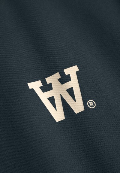 Tissu bleu foncé avec une surface texturée présentant un grand logo couleur crème et un symbole de marque déposée.