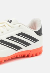 Scarpa da calcio bianca con righe nere e suola in gomma arancione. Presenta una tomaia testurizzata con rivestimento in rete e chiusura tradizionale con lacci.