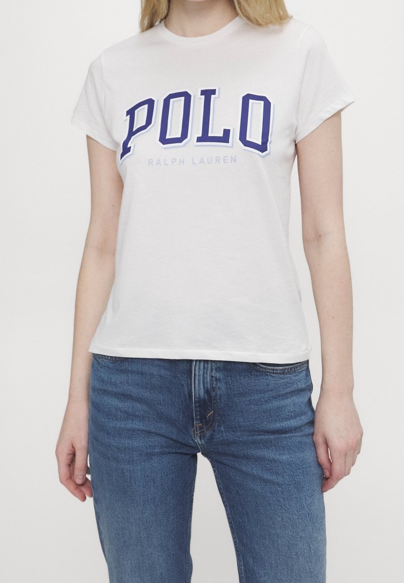 Vit T-shirt i bomull med korta ärmar, med en blå "POLO"-logotyp och texten "Ralph Lauren" tryckt nedan i ljusare blått.