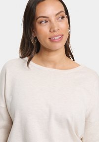 Maglione leggero color beige chiaro con scollo a barca e texture a coste sulle maniche. Tessuto liscio e morbido con vestibilità comoda.