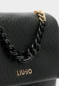Schwarze, strukturierte Lederhandtasche mit einem goldenen und schwarzen Kettenriemen, auf der Frontseite mit einem goldenen Logo "LIUJO".