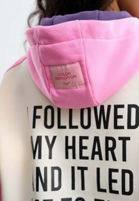 Bluza z kapturem z różowym kapturem, czarnym napisem „FOLLOWED MY HEART AND IT LED” oraz etykietą „COLOR REVOLUTION” na plecach.