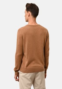 Brun, stickad tröja med rundad hals, raglanärmar och mjuk textur. Bärs över ljusbeiga byxor, vilket framhäver en avslappnad passform.