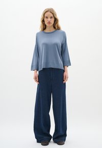 Svetlo modra oversize jopica s širokimi rokavi, v kombinaciji z ohlapnimi temnimi jeans hlačami. Gladka tekstura, sproščen dizajn in udoben kroj.