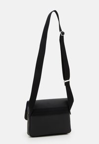 Svart messengerbag med en teksturert stoffeksterior, rektangulær form, justerbar nylonrem og hardware i sølvfarge.