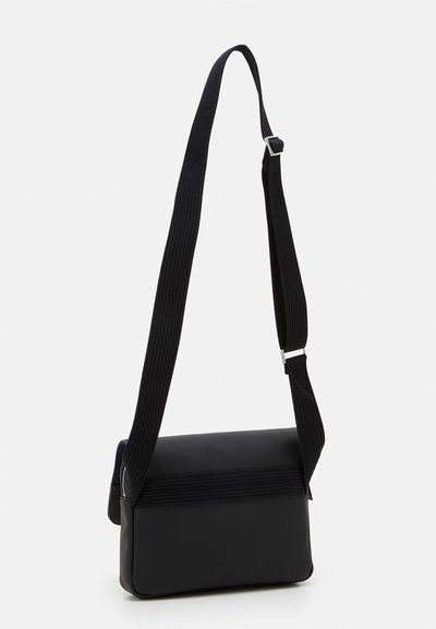 Sac messager noir avec un extérieur en tissu texturé, de forme rectangulaire, une bandoulière en nylon réglable et des accents en métal argenté.