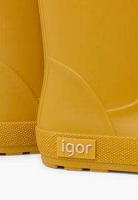 Bottes en caoutchouc jaunes avec une semelle texturée et un dessus lisse. Le nom de la marque "igor" est embossé sur une étiquette latérale.