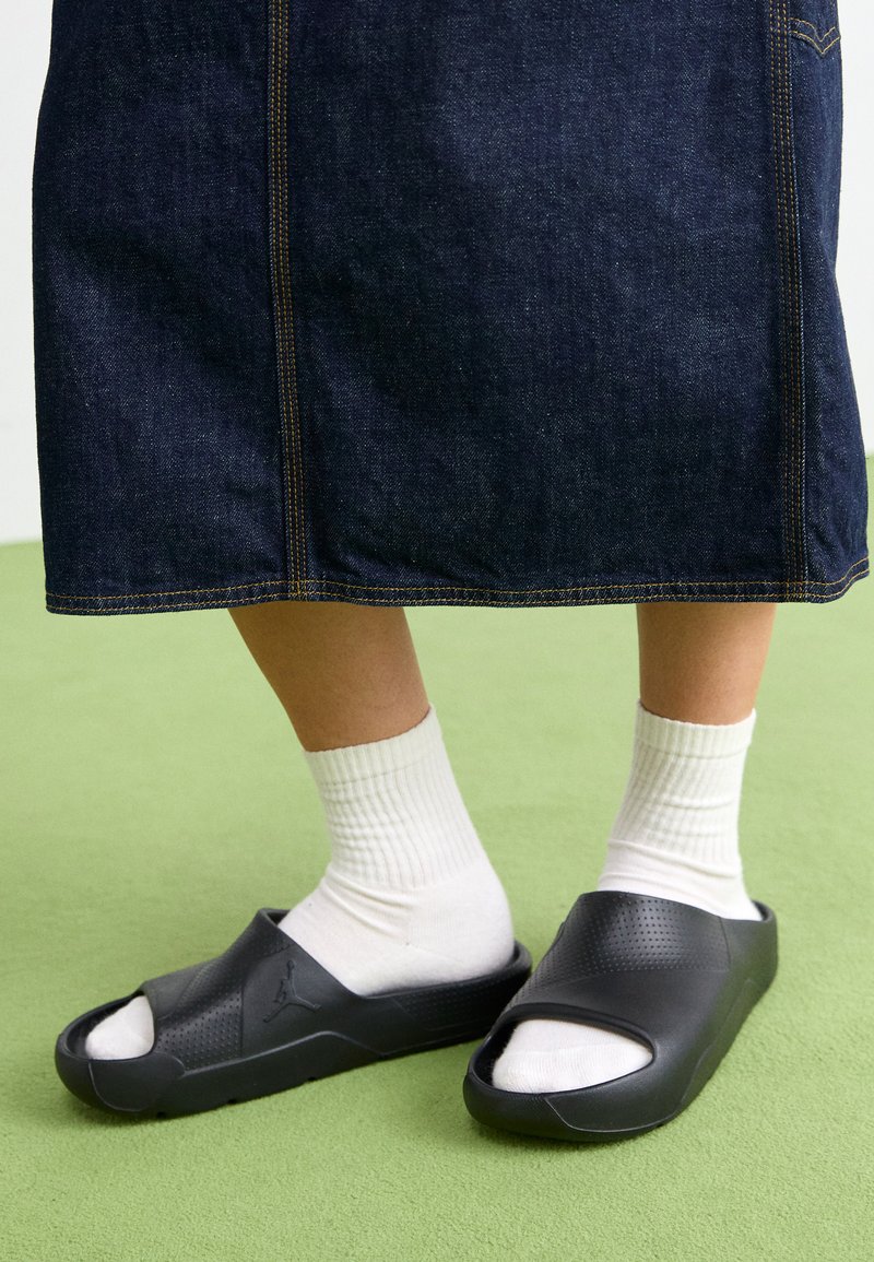 Infradito in gomma nera con design open toe, tomaia testurizzata e suola bianca. Indossati con calze bianche a coste e una gonna di jeans.
